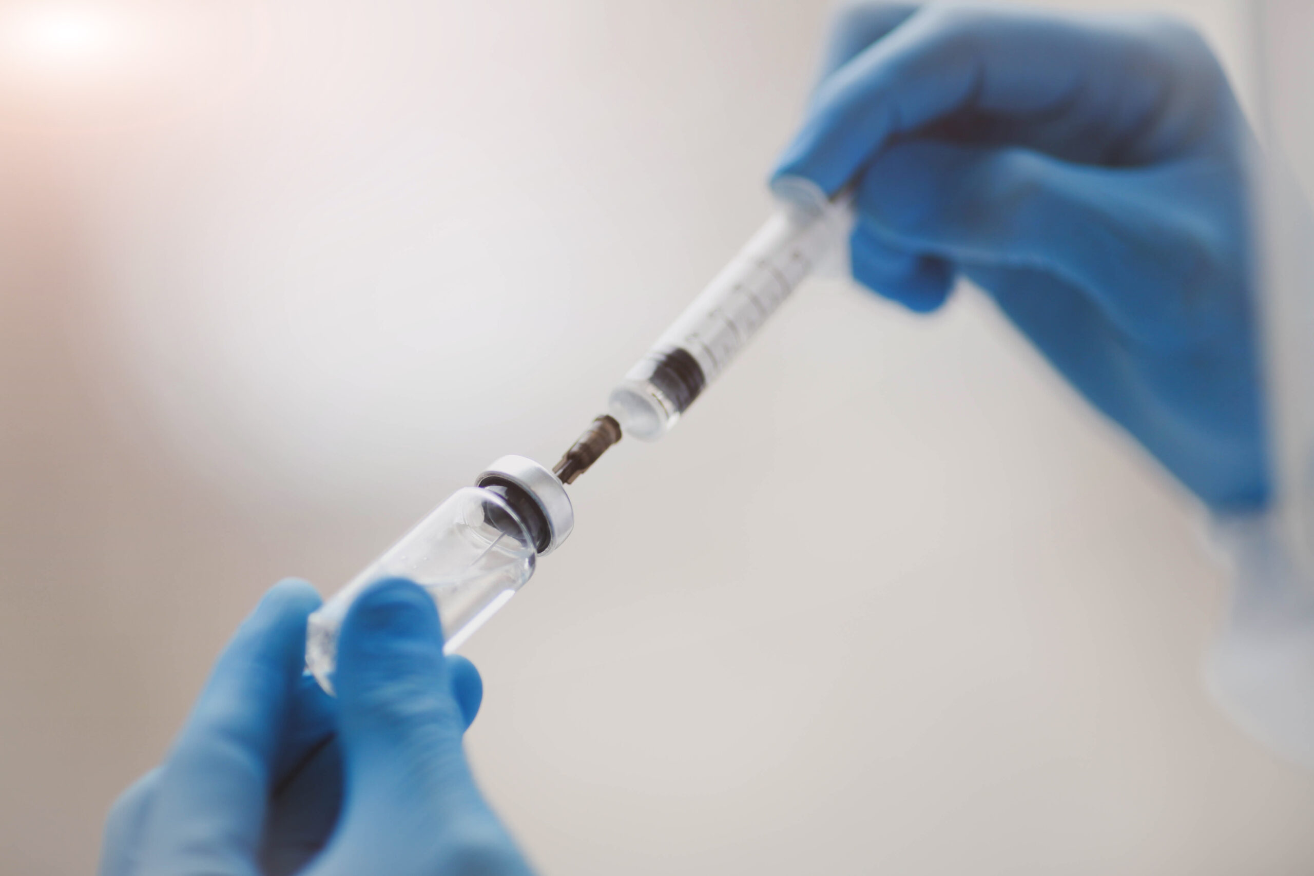 blue gloved hands inserting needle into sterile water for injection