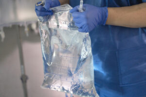 gloved hands holding a bag of sterile water